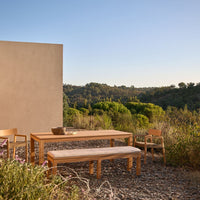Natural wood dining set with a light beige finish against a green hillside backdrop and clear blue sky.