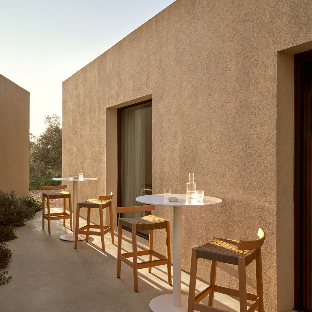 Natural beige walls with soft shadows, contrasting white tables, and light brown wooden bar stools.