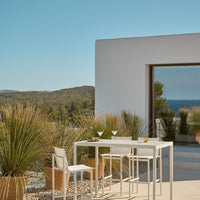 Modern white dining set against a serene blue sky and green hills, with soft natural tones in potted plants.