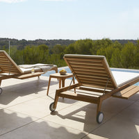 Two wooden lounge chairs with horizontal slat patterns in natural tones, set against a sunny outdoor background.
