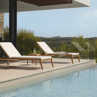 "Simple white lounge chairs with natural wood accents beside a tranquil blue pool, set against a green landscape."