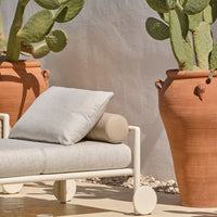 Light gray lounge chair with textured fabric, complemented by terracotta pots and lush green cactus plants.