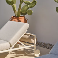 Light beige lounge chair with a textured fabric, set against a neutral background with a potted cactus.