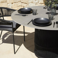 Round gray dining table with black plates and utensils, featuring textured black chair pattern, set against a stone backdrop.