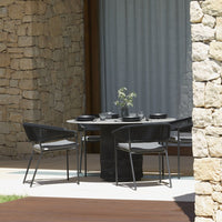 "Round black dining table with textured surface and sleek chairs against a natural stone backdrop and soft gray curtains."