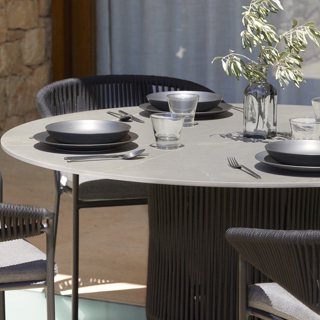 Modern round dining table with grey surface, black tableware, and textured black chairs, set against a natural stone backdrop.