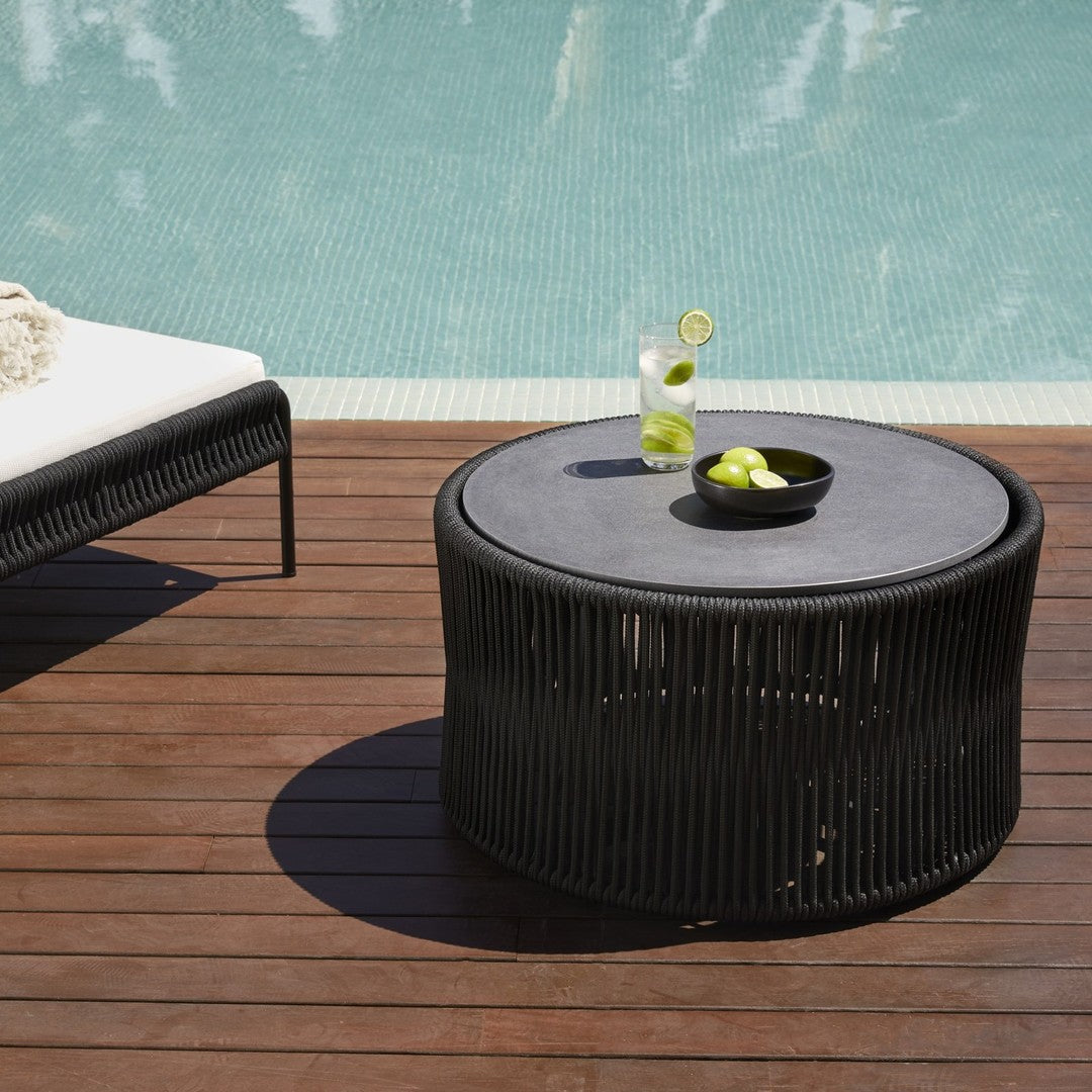 Black round coffee table with vertical slats, placed on a wooden deck near a pool, featuring black and green accents.