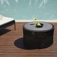 Black round coffee table with vertical slats, placed on a wooden deck near a pool, featuring black and green accents.