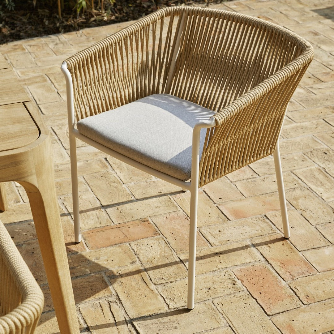 Tan woven chair with white cushion, featuring a modern, minimalist design on a rustic brick patio.