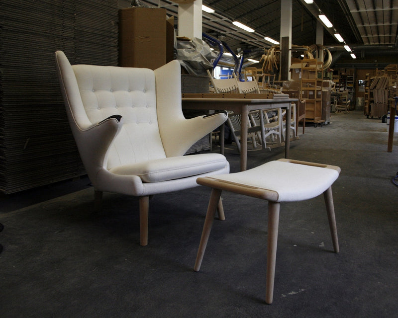 White modern armchair with a sleek design and natural wood legs, paired with a matching footstool.