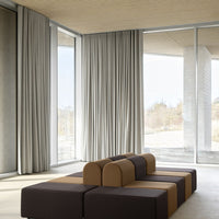 Geometric sofa in earthy tones of brown and beige, complemented by soft gray curtains in a modern interior setting.