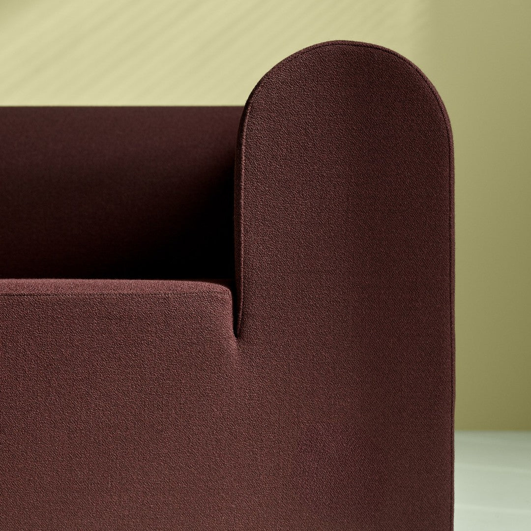 Dark burgundy fabric sofa corner against a soft pastel green background, featuring a smooth, minimalist design.