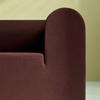 Dark burgundy fabric sofa corner against a soft pastel green background, featuring a smooth, minimalist design.