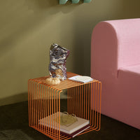 Orange wire cube side table next to a light pink sofa, featuring smooth, modern lines and contemporary design.