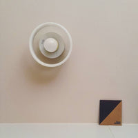 White circular light fixture against a beige wall next to a square tile with navy blue and tan geometric patterns.