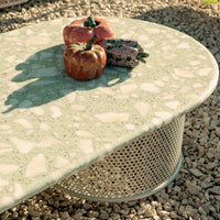 Green terrazzo coffee table with textured surface and circular metal base, accented by decorative pumpkins. 