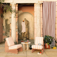 "Striped pink and white lounge chairs with a vibrant backdrop and subtle earthy tones, accented by green foliage."