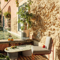 Gray striped chair with a red frame next to a round, green patterned table in a sunlit outdoor setting.