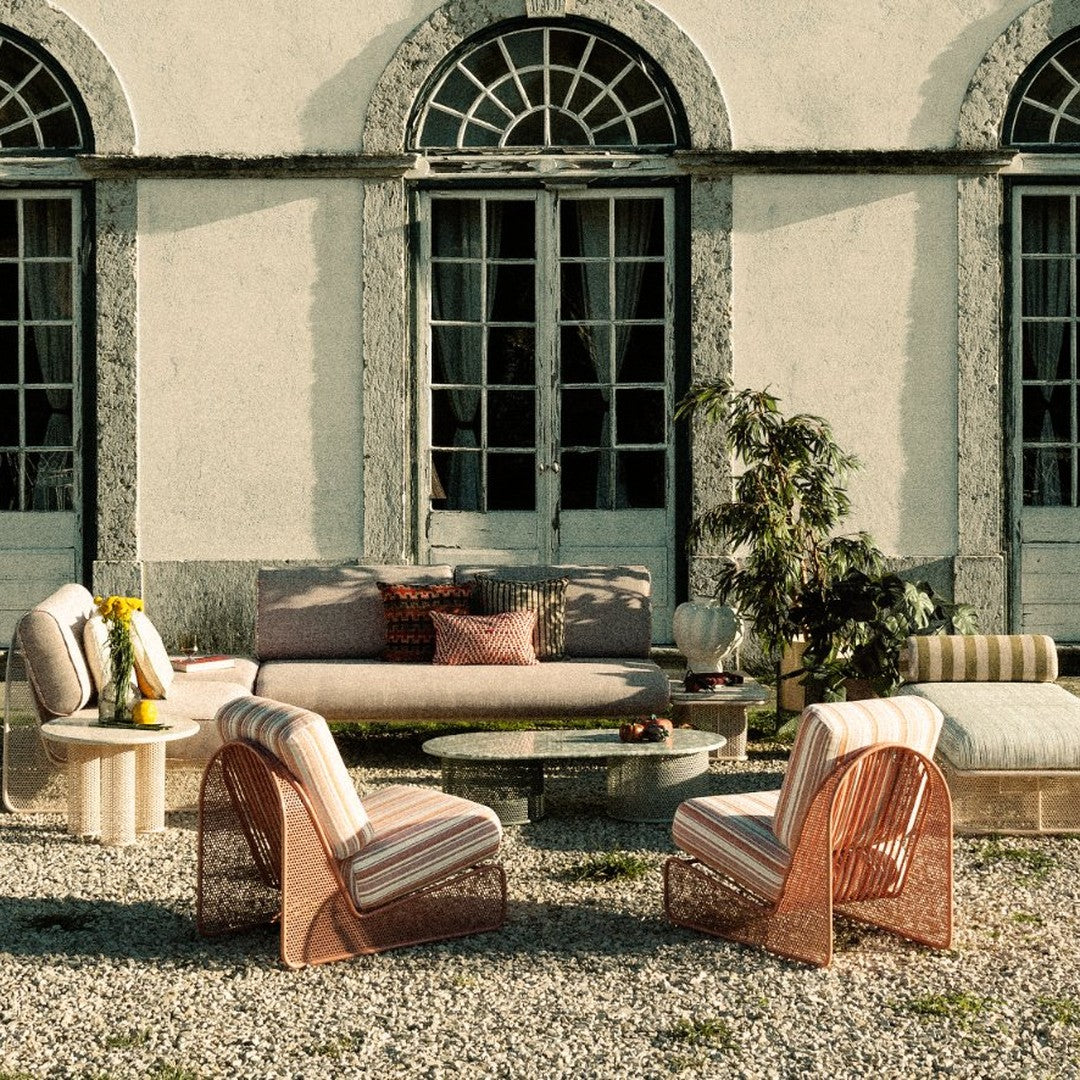 "Outdoor seating in muted tones with striped and textured patterns, surrounded by greenery and natural stone."