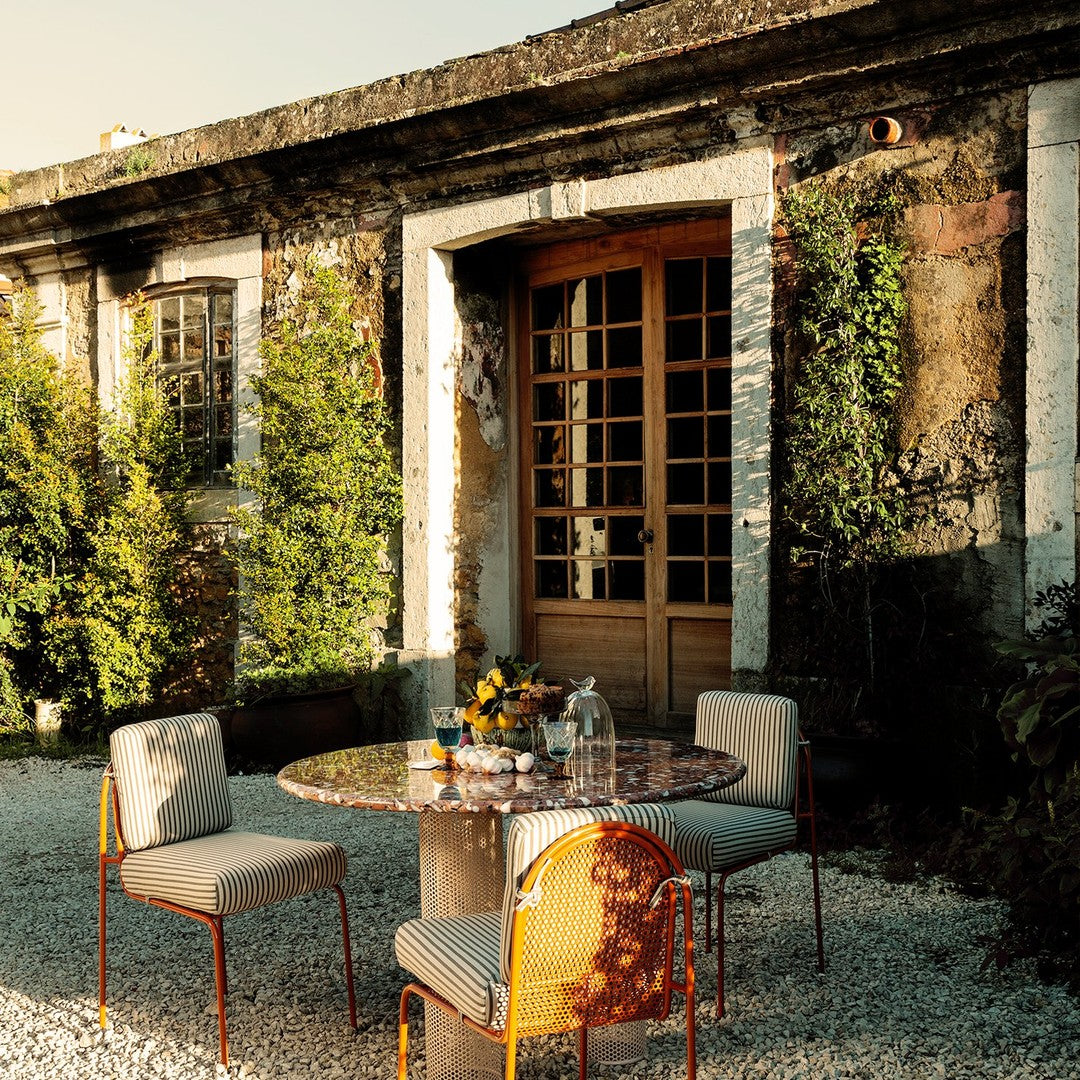 Patio dining set with vibrant floral-patterned cushions, neutral stone table, and warm metal accents in a lush garden setting.