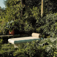 Striped cushion in beige and cream on a textured green lounging sofa amidst lush greenery and vibrant plants.