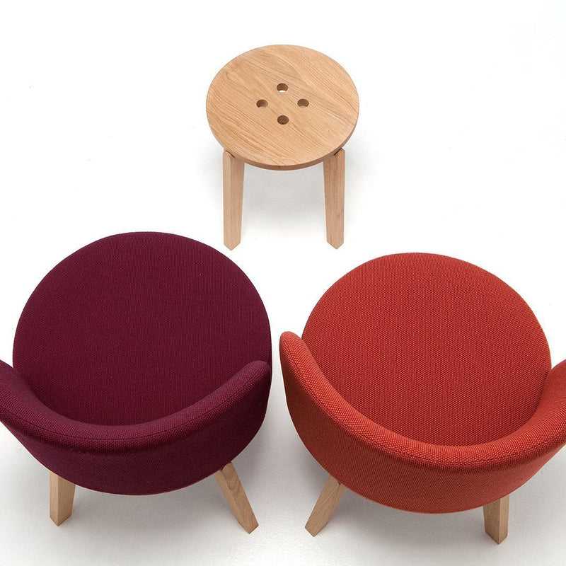 "Two plush chairs in deep plum and vibrant red, accompanied by a light wood stool against a white background."