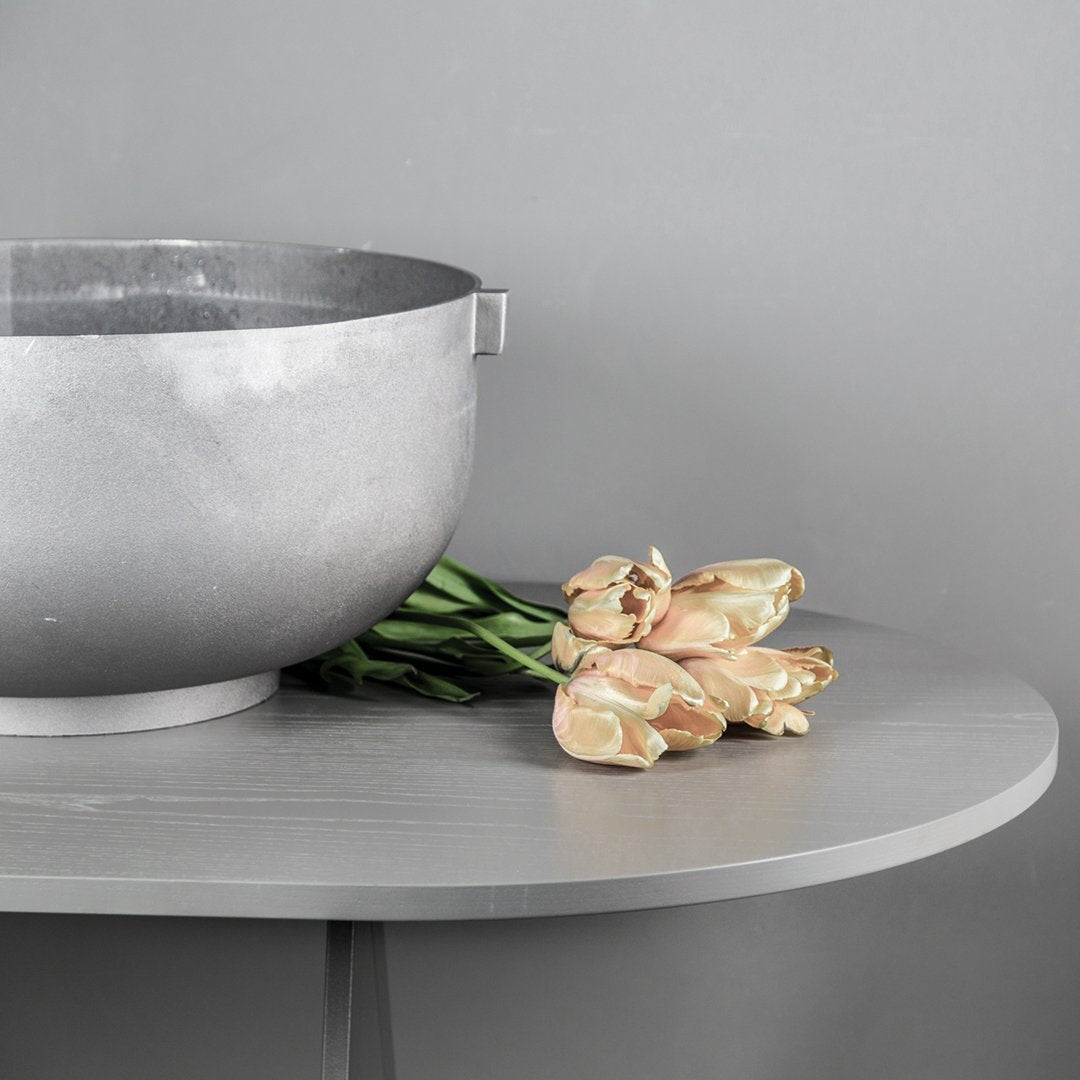 "Silver bowl and soft pink tulips on a sleek gray table, creating a modern and elegant visual contrast."