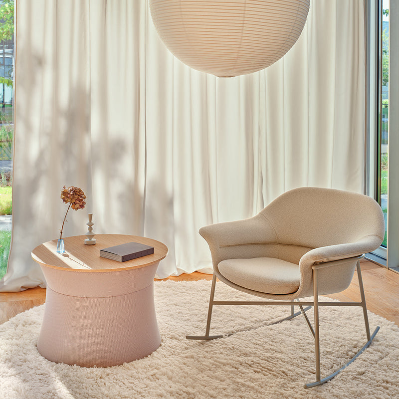 Soft beige chair and light pink accent table on a textured cream rug with airy white drapes in a bright, sunlit room.