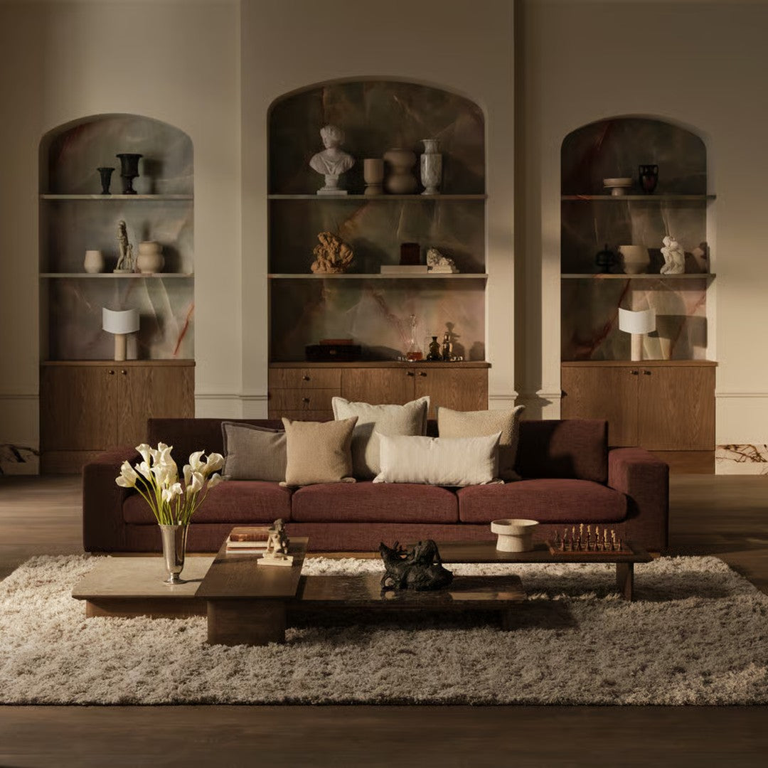 Brown velvet sofa with cream and beige cushions, set against a minimalist backdrop of warm tones and textured patterns.