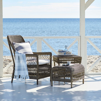 Woven brown wicker chair and table with a blue and white striped blanket and cushion by the beach.