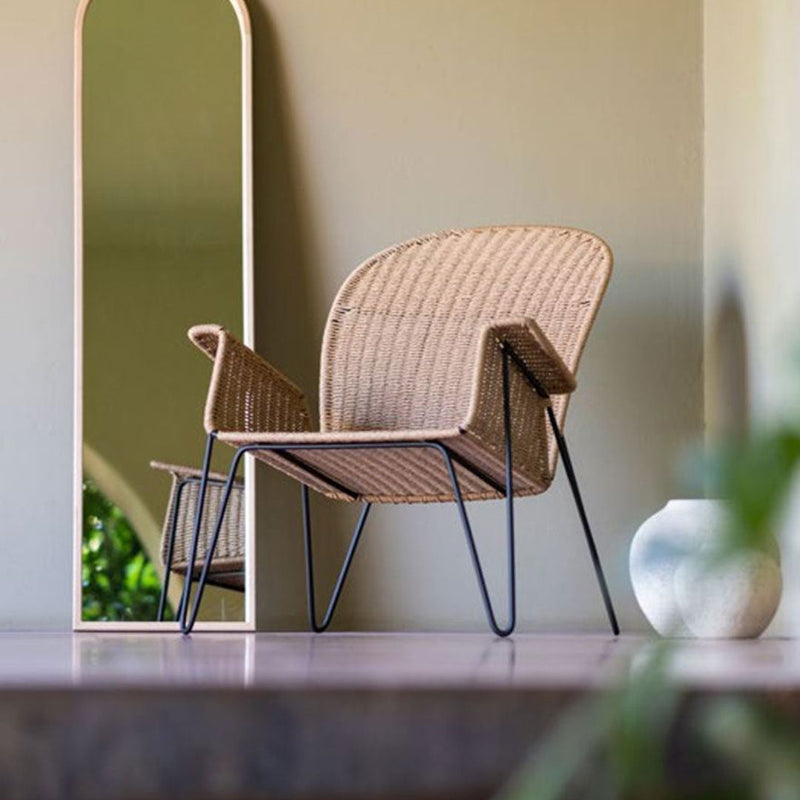 "Woven beige rattan chair with sleek black legs, set against a soft green wall, reflecting modern minimalist design."