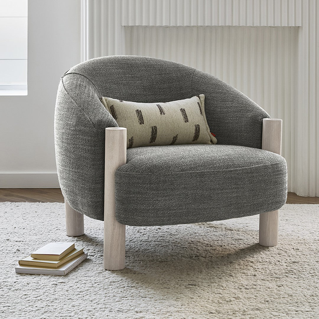 Gray upholstered armchair with a textured fabric and light wooden legs, featuring a patterned decorative pillow.