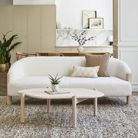 White curved sofa with light wooden legs, accented by neutral-toned cushions and a textured beige rug.
