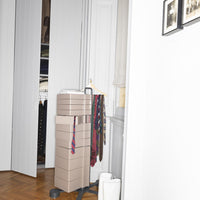 Stacked beige storage boxes with colorful patterned ties hanging beside, set against a white wall.