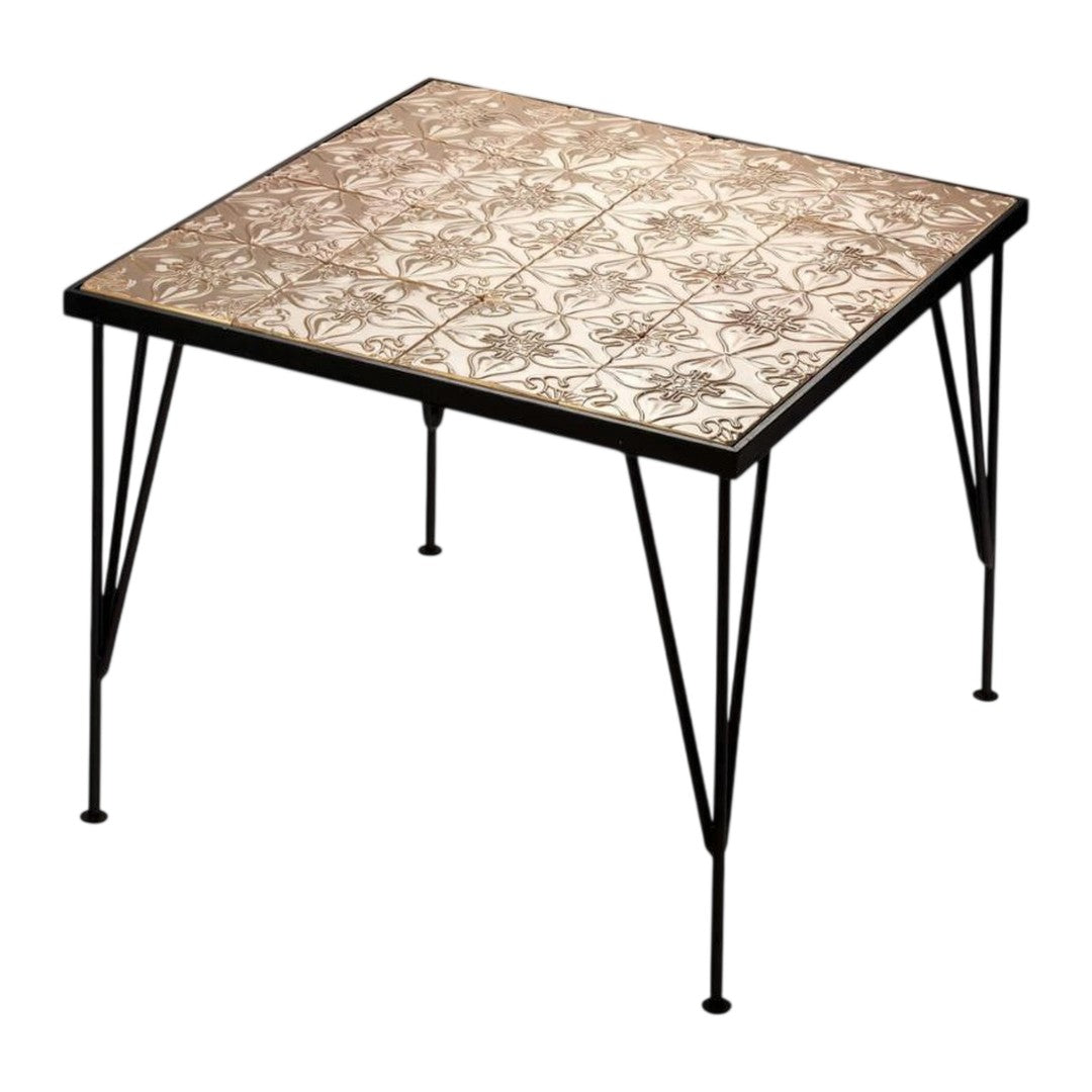 Square table with intricate beige and cream floral tile pattern on a black metal base. Ideal for modern decor.