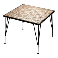 Square table with ornate beige tile top and black metal legs, featuring intricate floral patterns.