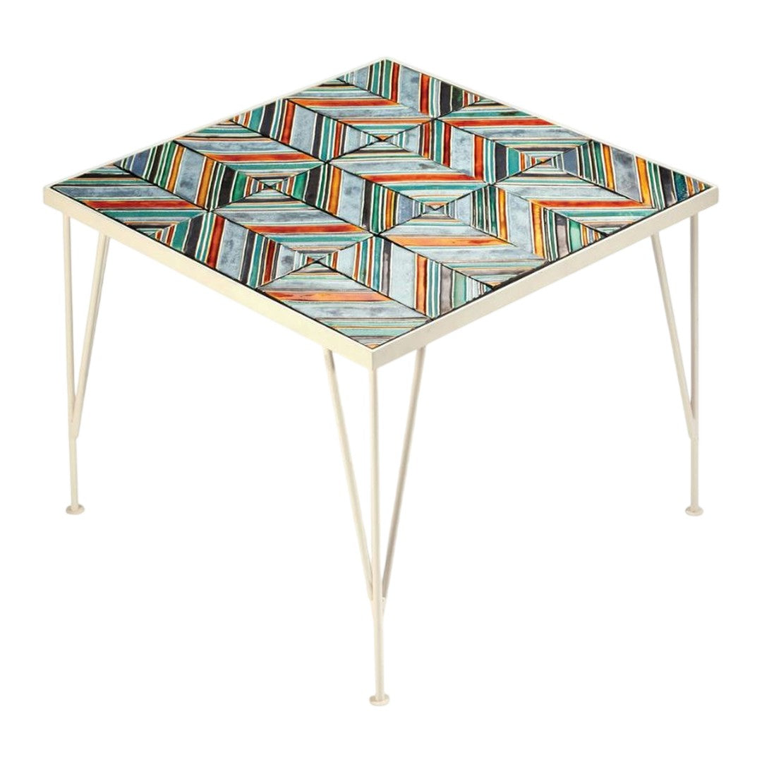 Square table with colorful geometric pattern in orange, blue, and white, complemented by metal legs.