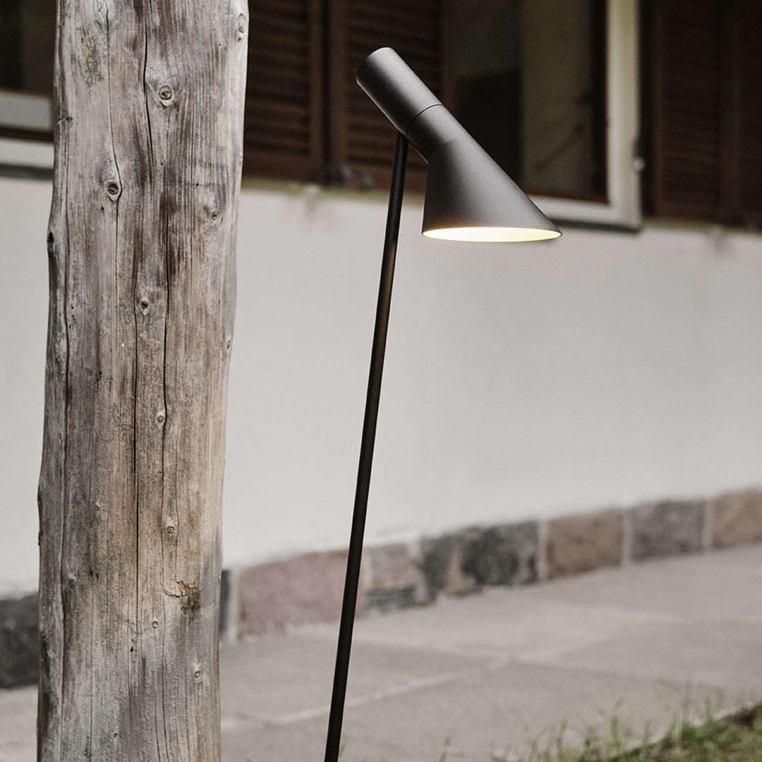 Sleek black floor lamp with a conical shade, set against a rustic wooden post and neutral-toned wall.