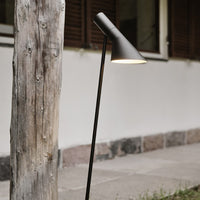 Sleek black floor lamp with a conical shade, set against a rustic wooden post and neutral-toned wall.