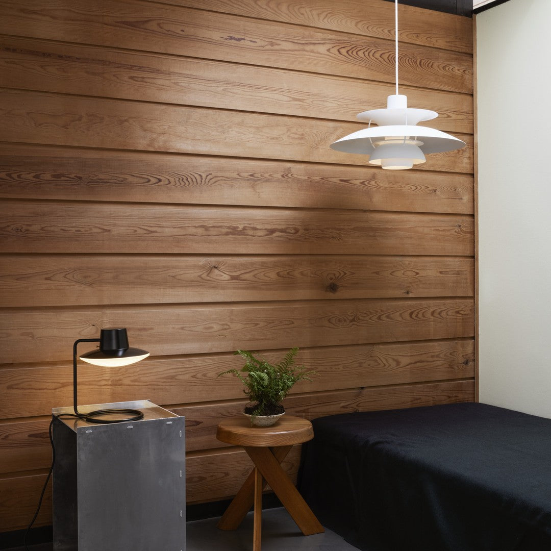 Modern bedroom with warm wood paneling, sleek black bedding, and minimalist white pendant light.