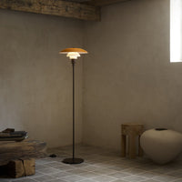 Minimalist floor lamp with a warm orange top and sleek black base, set in a neutral-toned room with earthy textures.