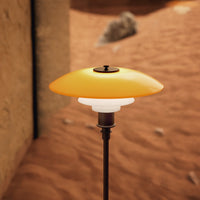 Stylish lamp with a smooth yellow and white glass shade, set against a sandy, rustic background.