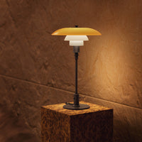 "Modern table lamp featuring a layered design with orange, white, and black elements against a warm, textured wall."