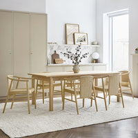 Light wood dining table with natural fiber chairs on a soft cream rug against neutral-toned walls.