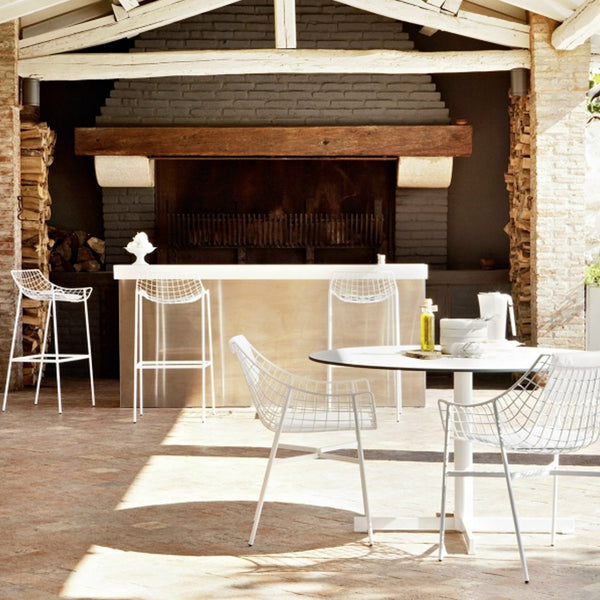 White wire chairs and table against a rustic stone background, featuring natural wood accents and warm earth tones.