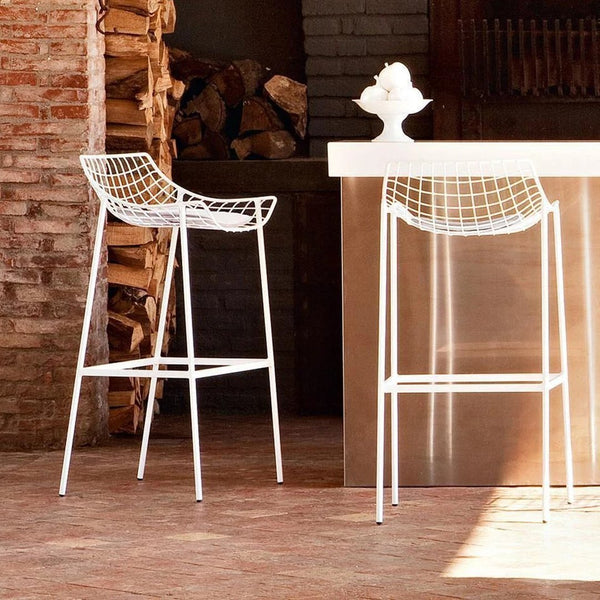 White wire bar stools with a modern geometric pattern against a rustic backdrop. Ideal for stylish indoor spaces.