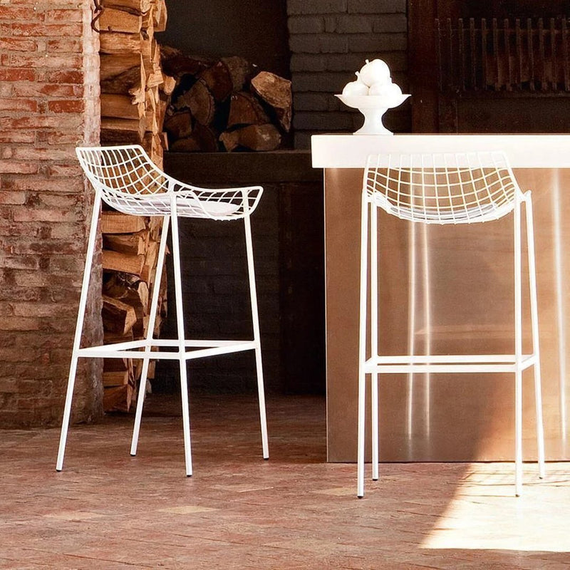 White wire bar stools with a modern geometric pattern against a rustic backdrop. Ideal for stylish indoor spaces.