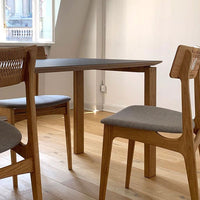 Modern wooden table with light oak finish, accompanied by gray upholstered chairs and a smooth natural wood floor.