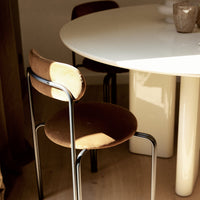 Brown velvet chair with a circular seat and backrest, metal frame, next to a white table in a warm, sunlit setting.
