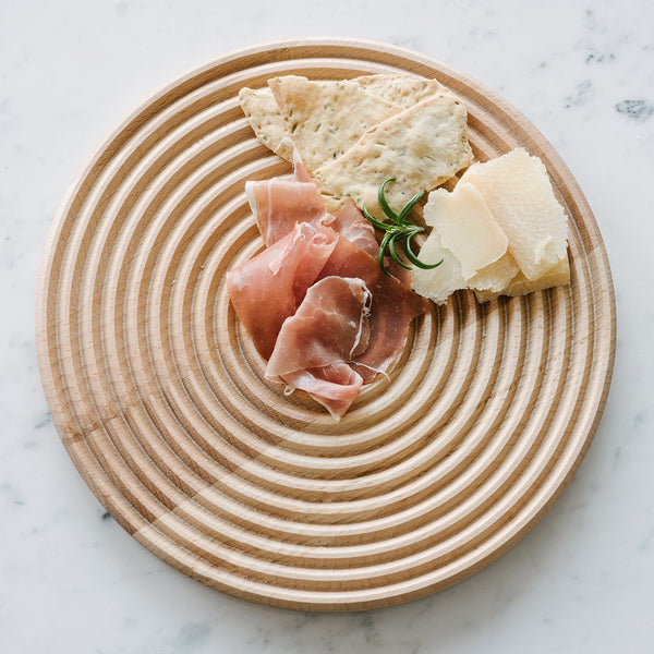 Natural wood plate with concentric circular grooves, featuring light beige tonal elements, ideal for serving snacks.